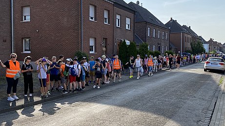 Auch hier sieht man die lange Schlange auf dem Bürgersteig. Alle winken in die Kamera. 